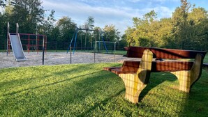 Un parque con un área de juegos, una banca y césped.