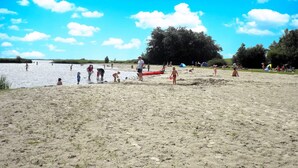 Una playa arenosa con gente realizando diversas actividades, un árbol grande y tiendas de campaña al fondo.