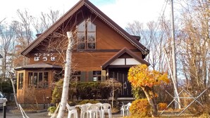 A wooden cabin with a gabled roof, a large window, and a small porch area with chairs.