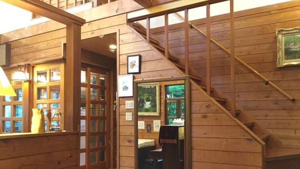A wooden interior with a staircase, wooden walls, and a mirror reflecting a room with a chair and table.