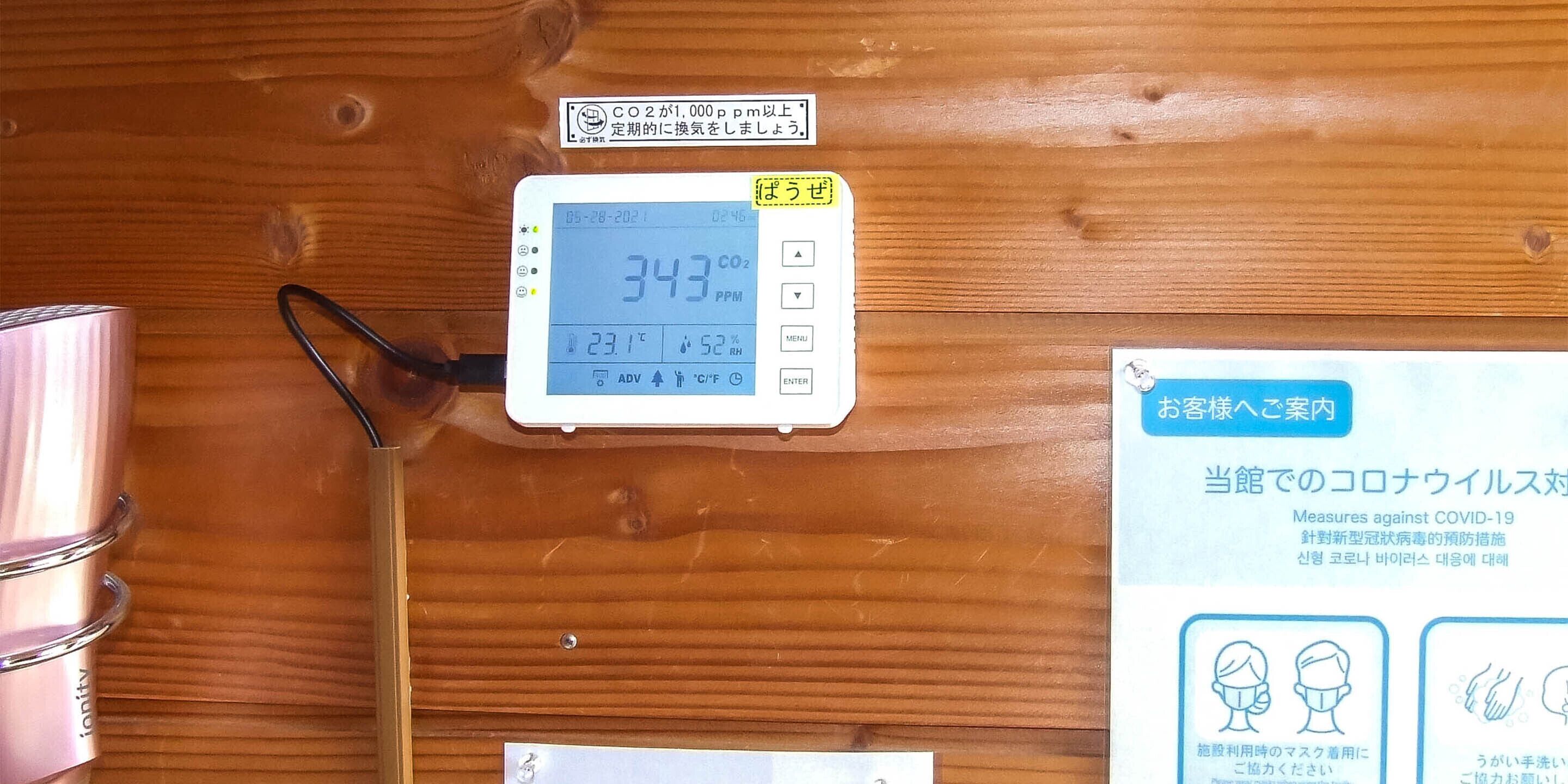 Un monitor de CO2 que muestra 343 ppm, un letrero con texto en japonés y un cartel con medidas de seguridad contra el COVID-19.