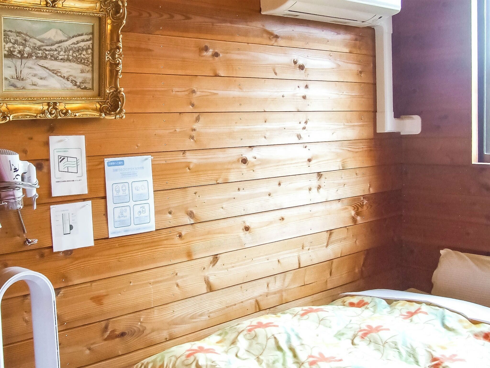 Ein Zimmer mit Holzwänden, einem Bett, einem gerahmten Bild und Papieren an der Wand.