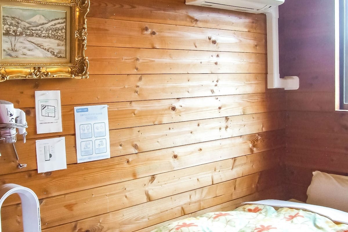 Een kamer met houten lambrisering, een bed, een lijst met een afbeelding en wat papieren aan de muur.