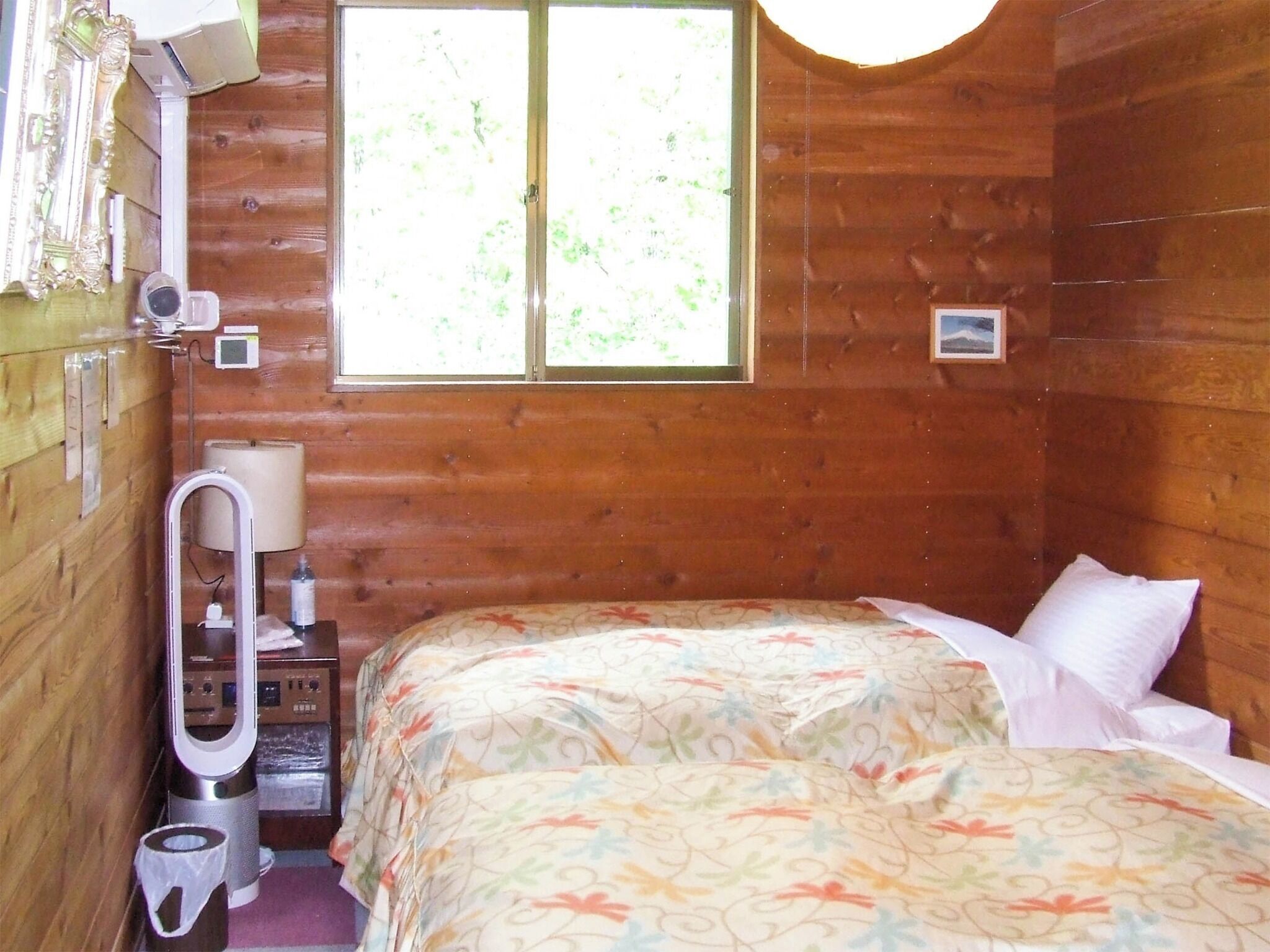 Ein Zimmer in einer Holzhütte mit einem Bett, einem Fenster, einem Heizgerät und einem kleinen Tisch.