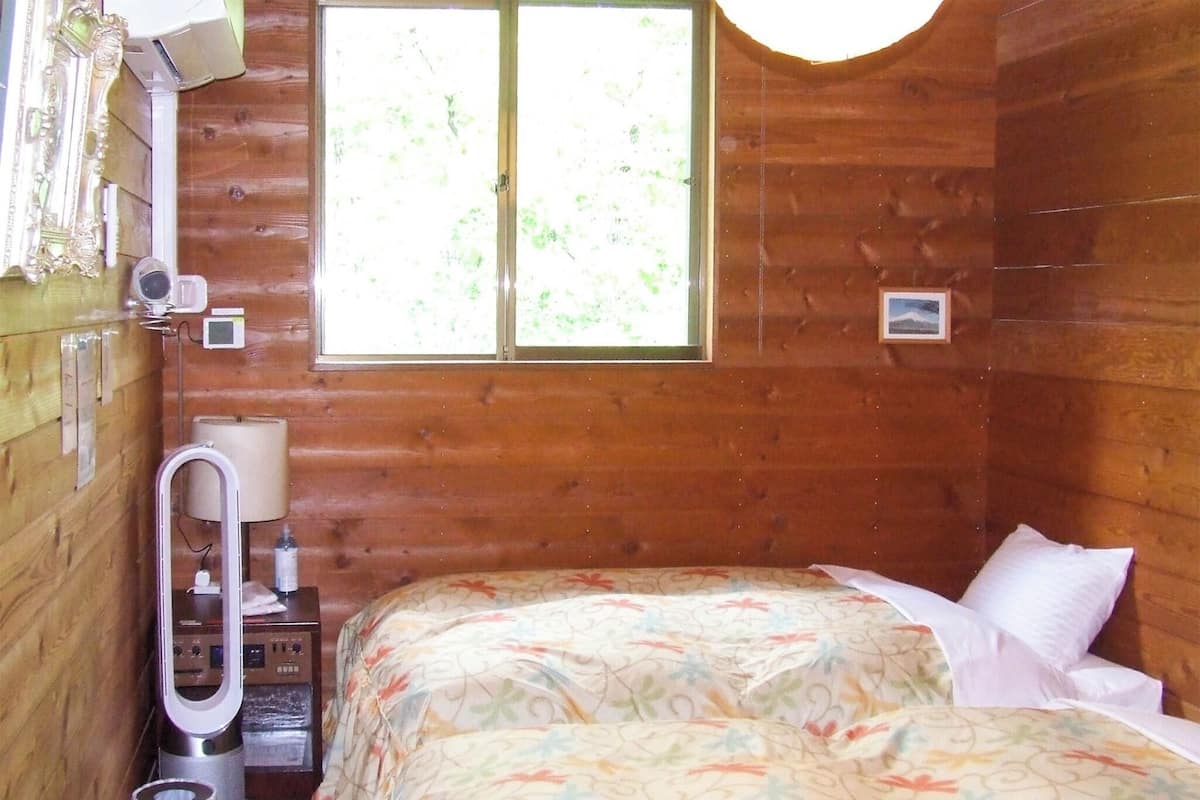 Een houten kamer met een bed, een raam, een kachel en een kleine tafel.