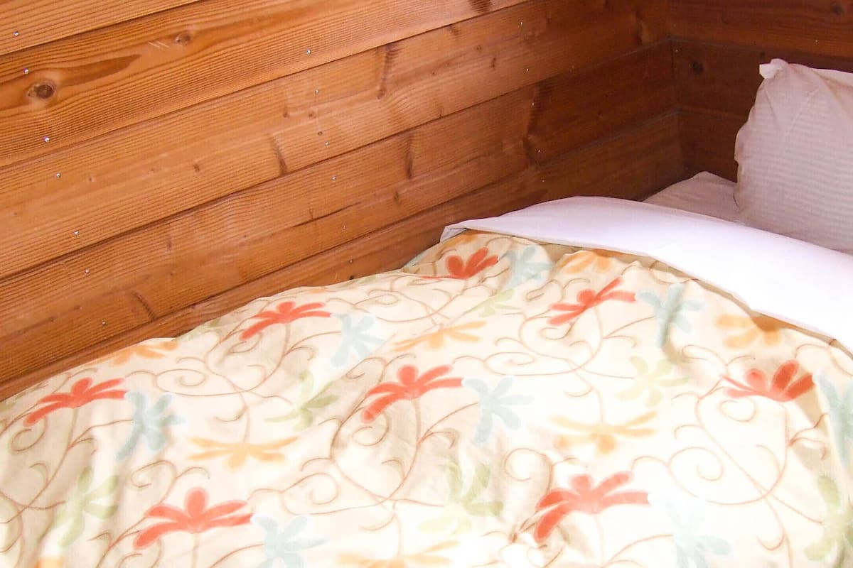 Een klein bed met een deken met bloemenmotief en een wit kussen in een houten kamer.