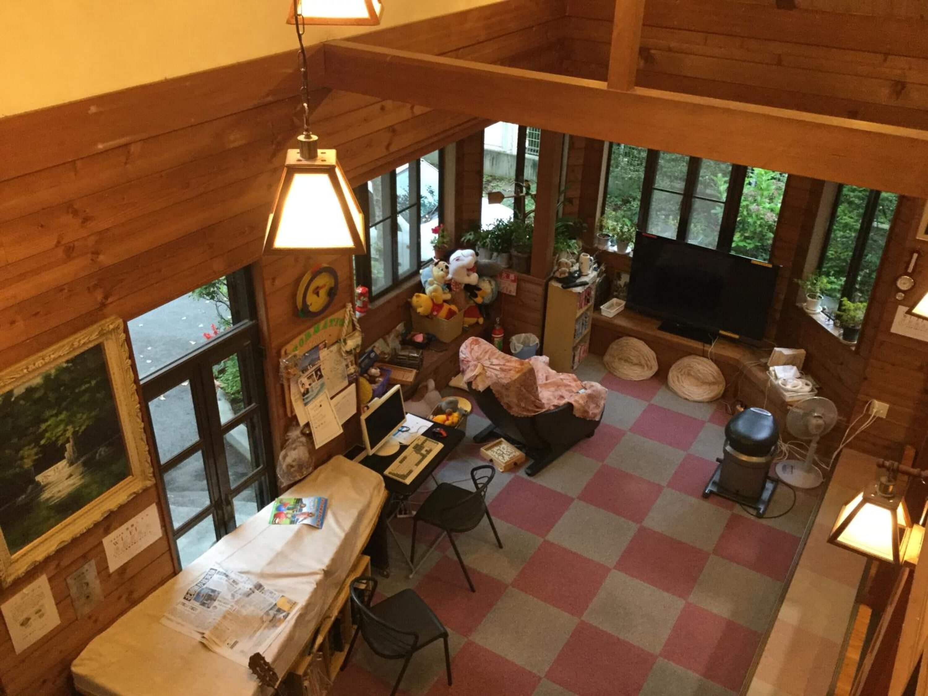 A cozy cabin-style room with a checkered floor, wooden walls, a dining area with a table and chairs, a television, and a window overlooking greenery.