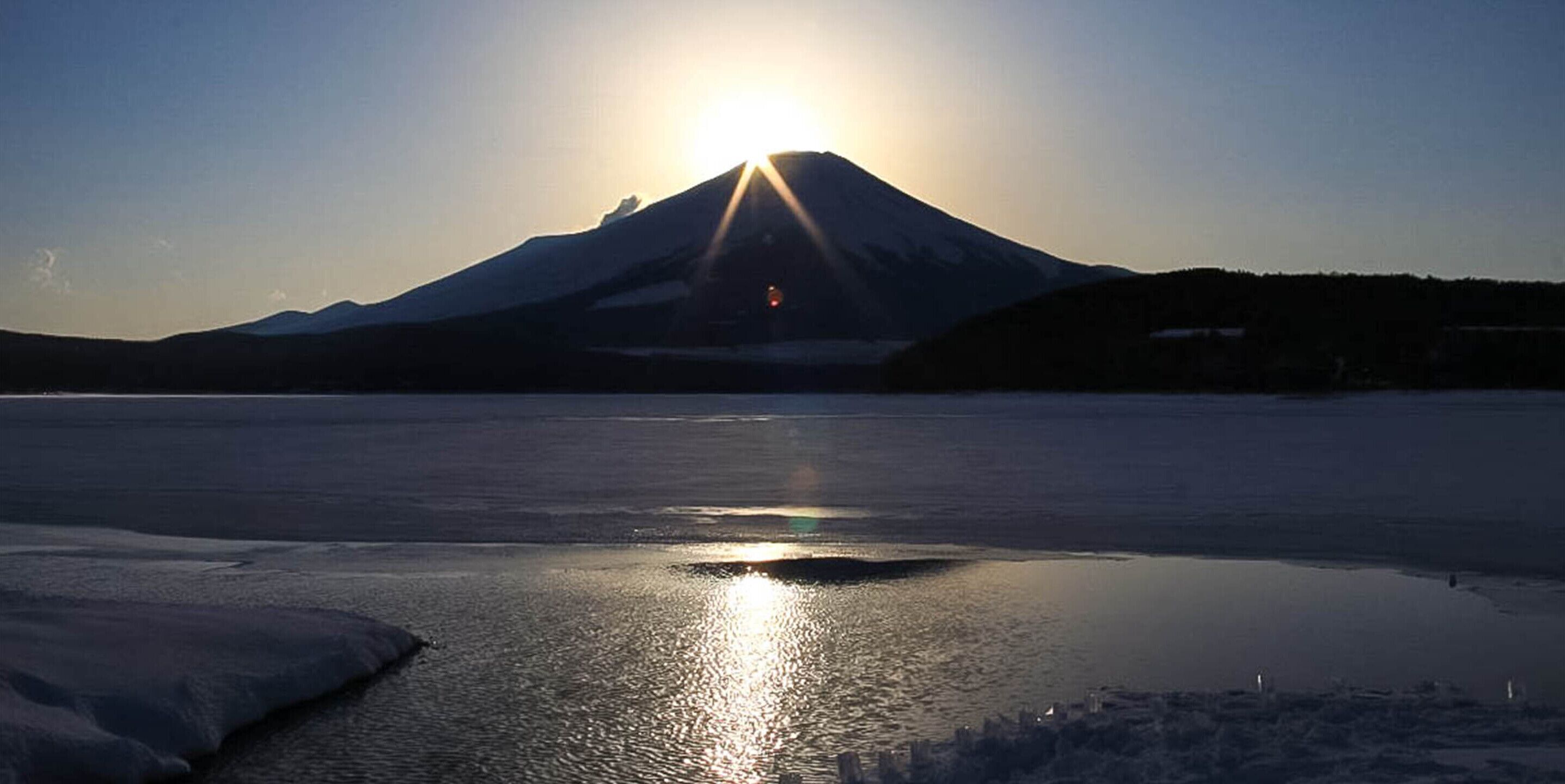 Ein Berg mit untergehendem oder aufgehendem Sonnenuntergang, der sich in ruhigem Wasser spiegelt.