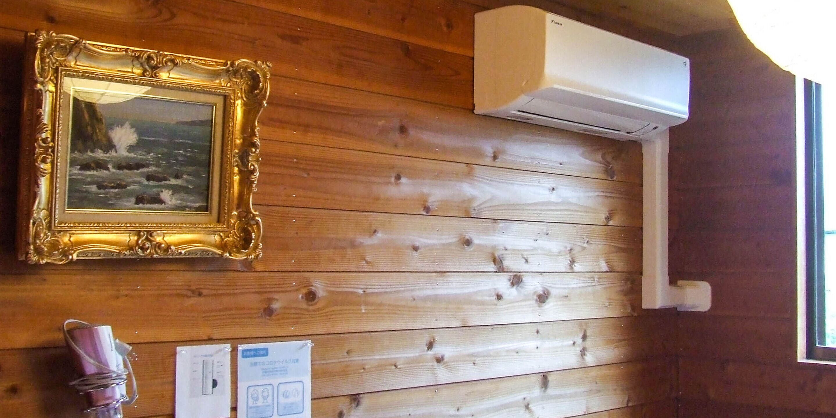 A wooden wall with a framed picture, an air conditioning unit, and some documents.