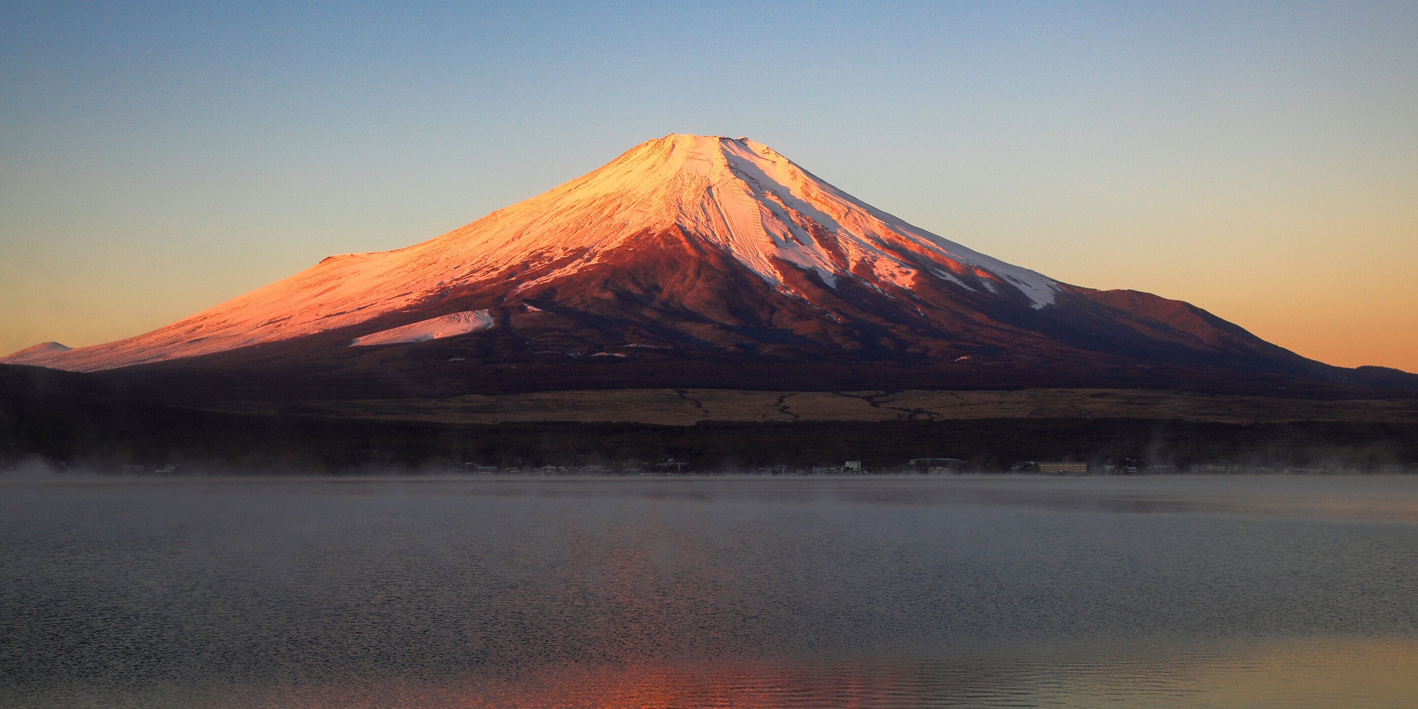 A mountain with a snow-capped peak and a calm lake in the foreground.