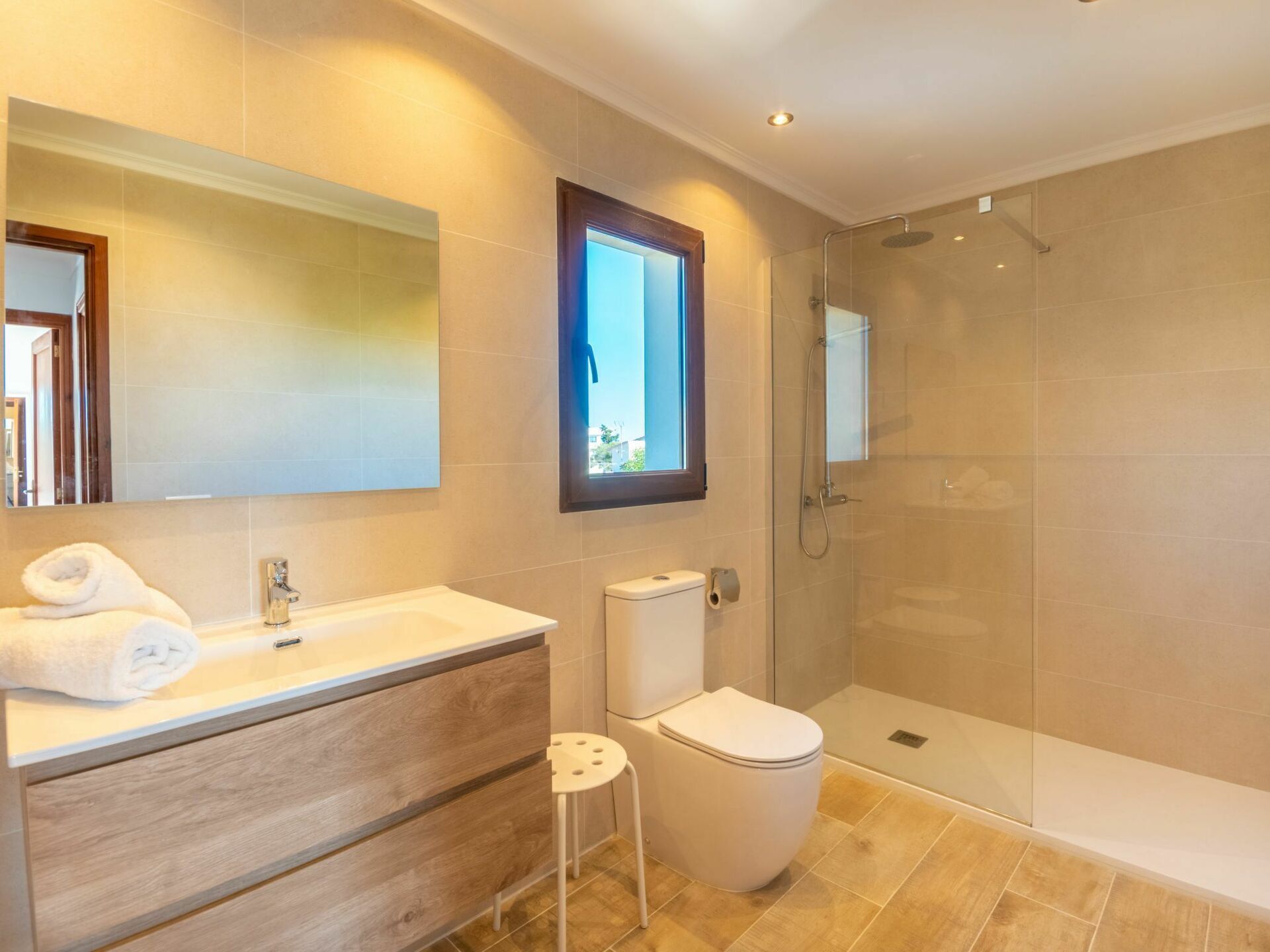 A modern bathroom with a large mirror, a vanity with a towel, a toilet, and a glass-enclosed shower area.