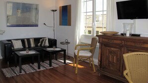 A living room with a sofa, a dining table, a TV, and a window with curtains. - Lovely apartment for 4 guests with WIFI, TV and terrace (Mimizan)