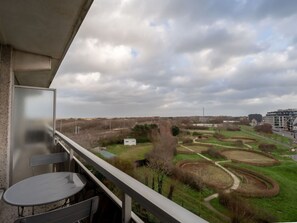 A balcony with a table and chairs, overlooking a landscaped garden with winding paths and a distant view of a cityscape.