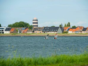 A waterfront view with windsurfers, houses, and a tower in the background.