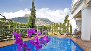 A swimming pool with a view of mountains, surrounded by a white building with a balcony and lounge chairs. - Beautiful  villa for 6 people with WIFI, private pool, TV, terrace and panoramic view (Calpe)