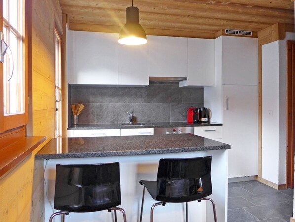 A modern kitchen with a granite countertop, stainless steel sink, and two black bar stools.