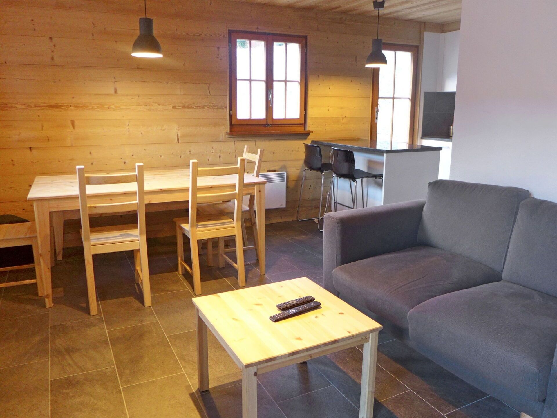 Un salon chaleureux avec une table à manger en bois, des chaises, un canapé gris et une petite table basse en bois.