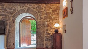 A stone-walled hallway with a wooden door leading outside, a wooden cabinet with a lamp, and a clock on the wall. - Wonderful private villa with WIFI, private pool, hot tub, A/C, TV, patio and pets allowed (Rijeka)