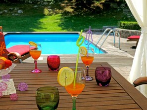 Mesa à beira da piscina com bebidas e frutas, com vista para a piscina.