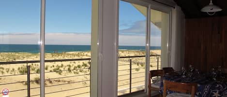 A room with a view of the beach, a dining table with chairs, and a ceiling fan.