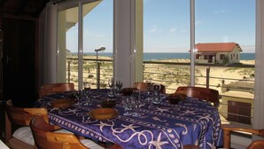 A dining area with a table set for four, large windows offering a view of the beach and ocean, and a ceiling light fixture. - Nice apartment for 4 guests with WIFI, TV and balcony (Mimizan)