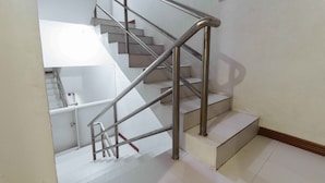 A staircase with metal railings and a handrail, leading to a landing with a white wall and a small shelf. - RedDoorz near Bambang Station (Manila)