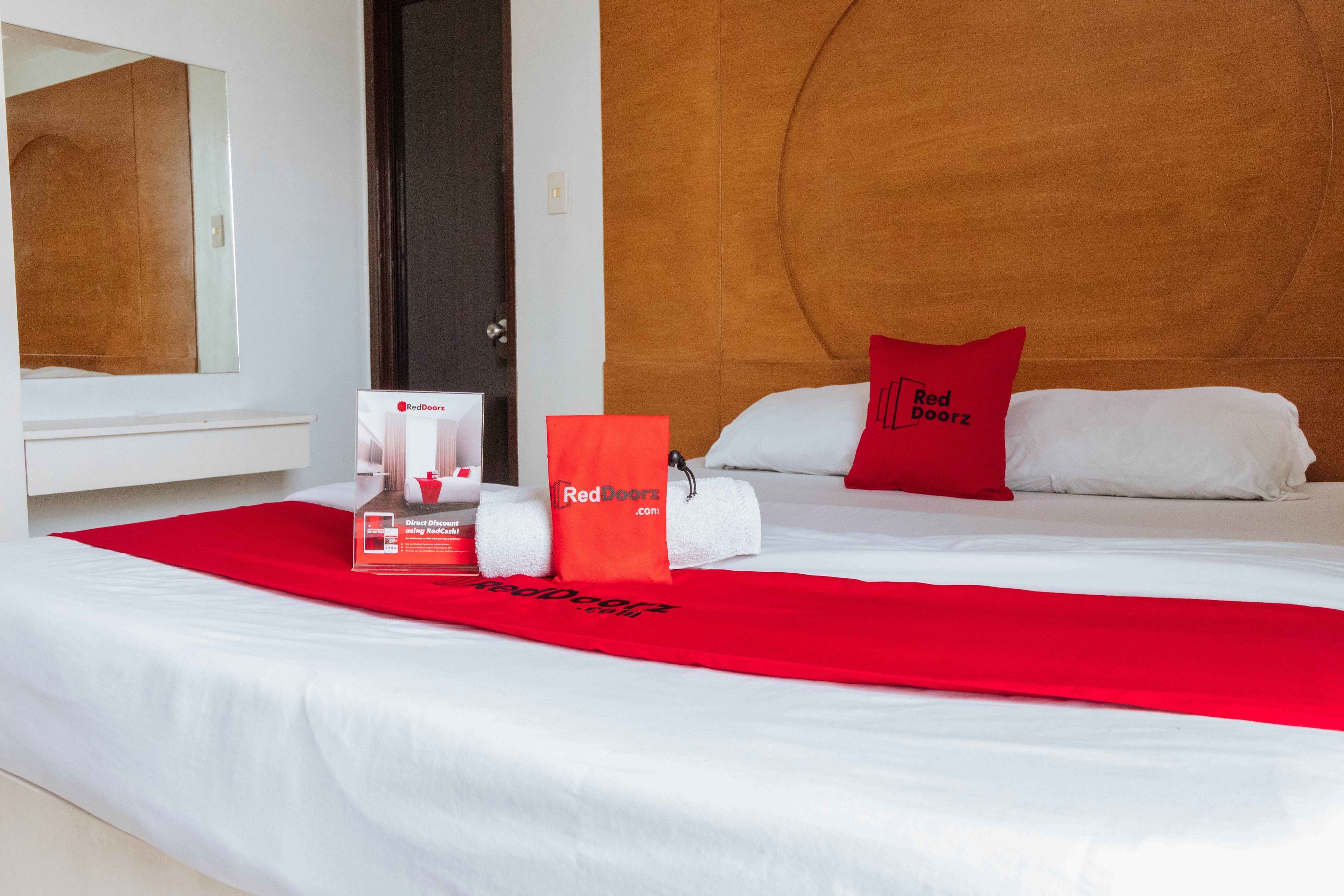 A hotel room with a bed, a red towel, a Red Doorz bag, and a Red Doorz sign.