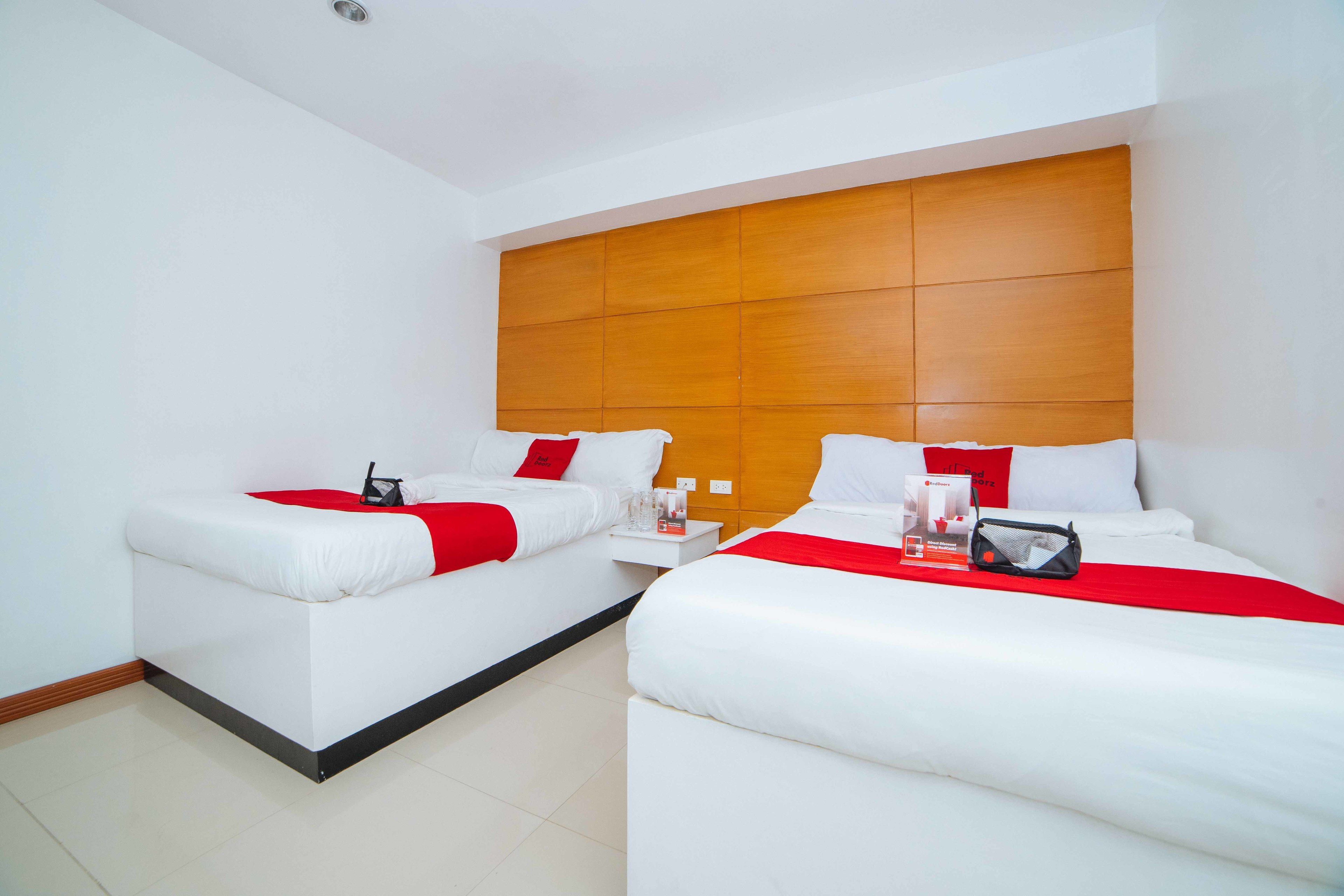 A hotel room with two beds, a wooden headboard, white bedding, and a red accent.