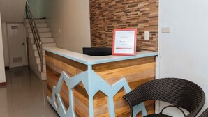 A reception desk with a wooden finish and a framed sign, a staircase, and a wicker chair. - RedDoorz near Bambang Station (Manila)
