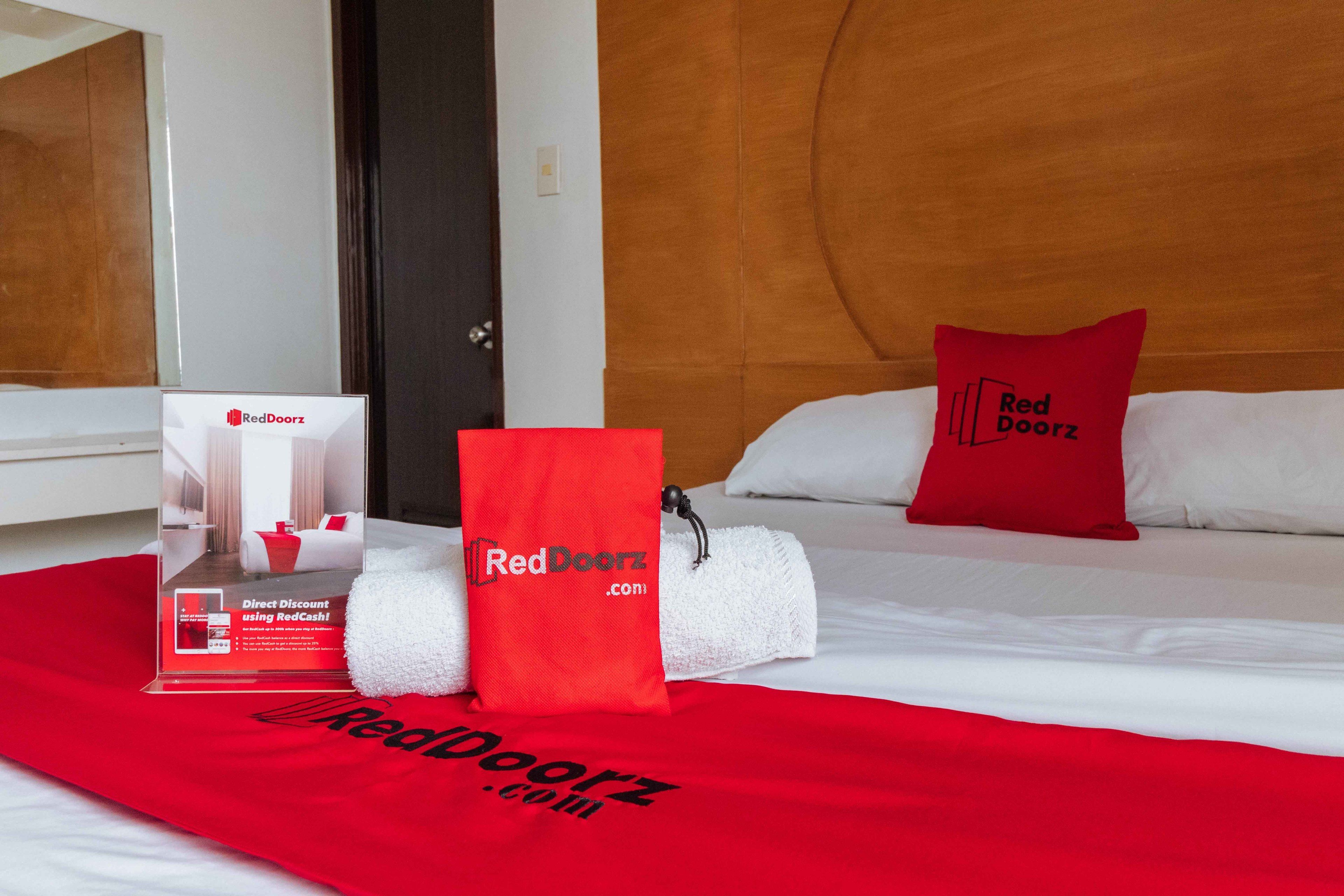Una habitación de hotel con una cama, una almohada roja, una toalla roja y un artículo promocional de RedDoorz.