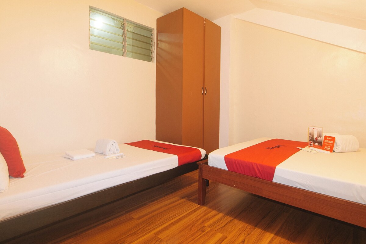 A hotel room with two single beds, wooden flooring, a wardrobe, and a window with blinds.