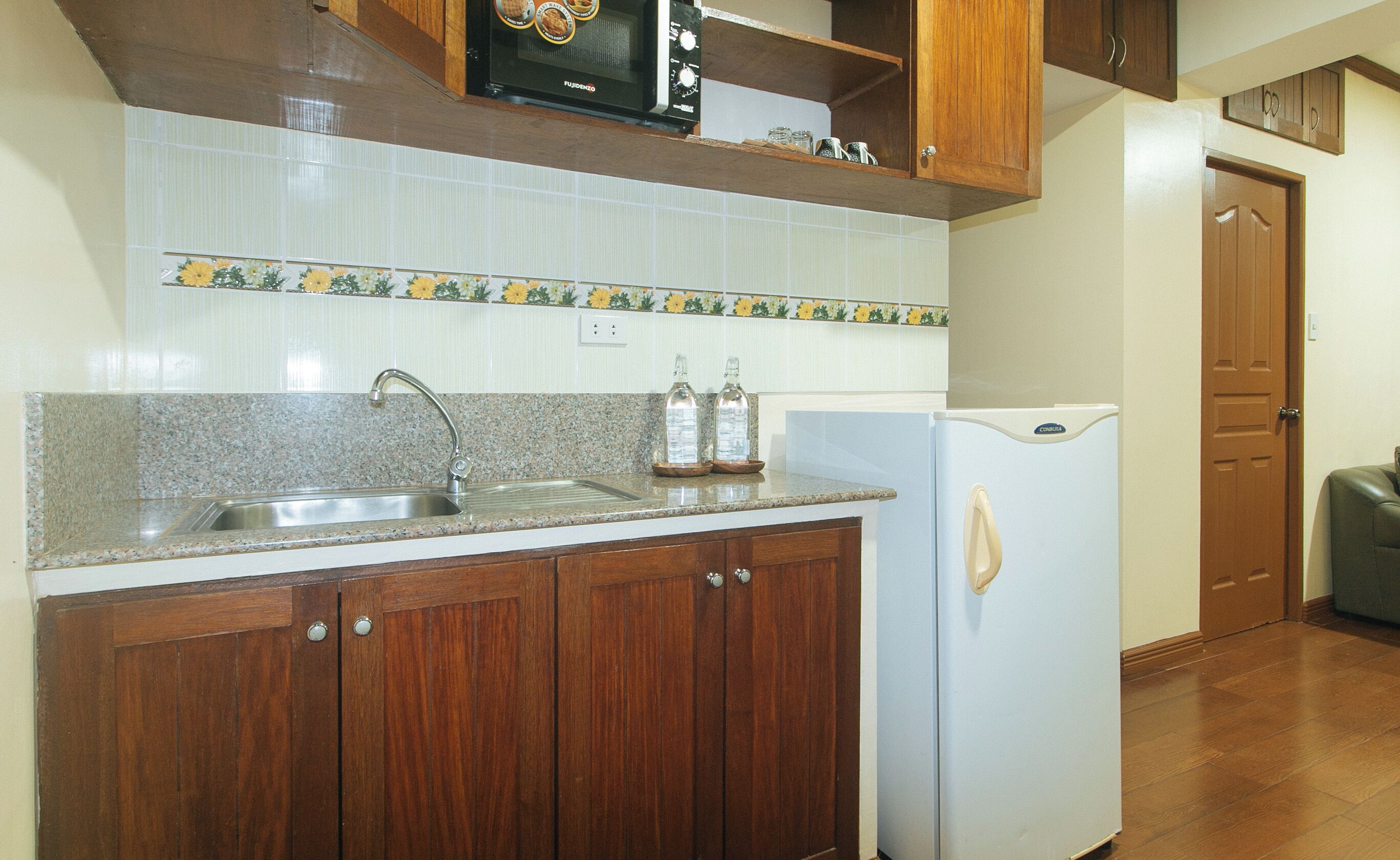 A kitchen with granite countertops, a stainless steel sink, wooden cabinets, a white refrigerator, and a microwave above the counter.