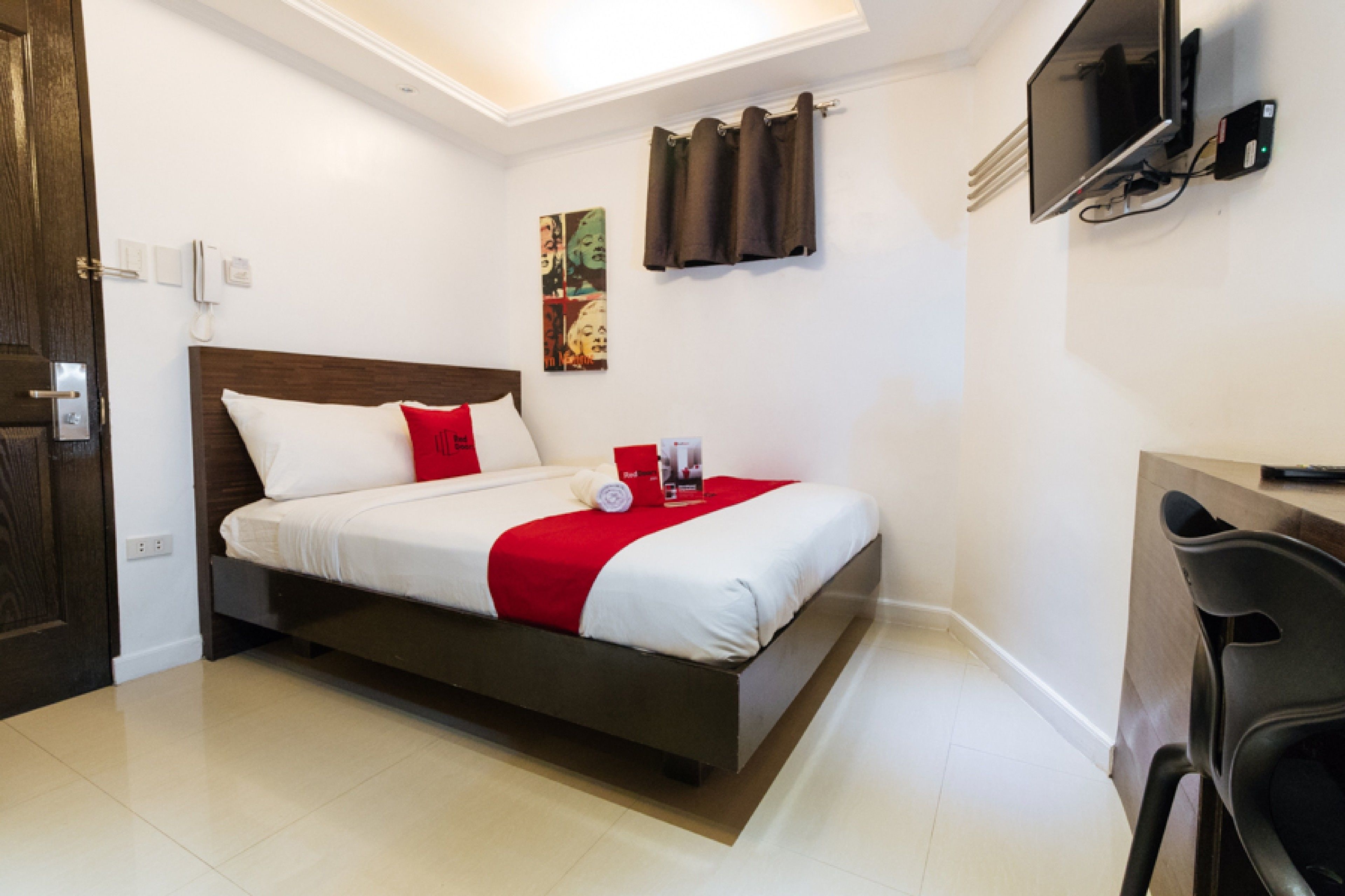 Une chambre d’hôtel avec un lit, un bureau, une chaise, une télévision et un tableau au mur.