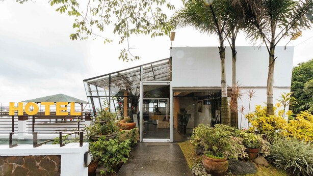 Una entrada de hotel moderna con fachada de vidrio, un camino que lleva a la puerta y diversas plantas en macetas alrededor de la entrada.
