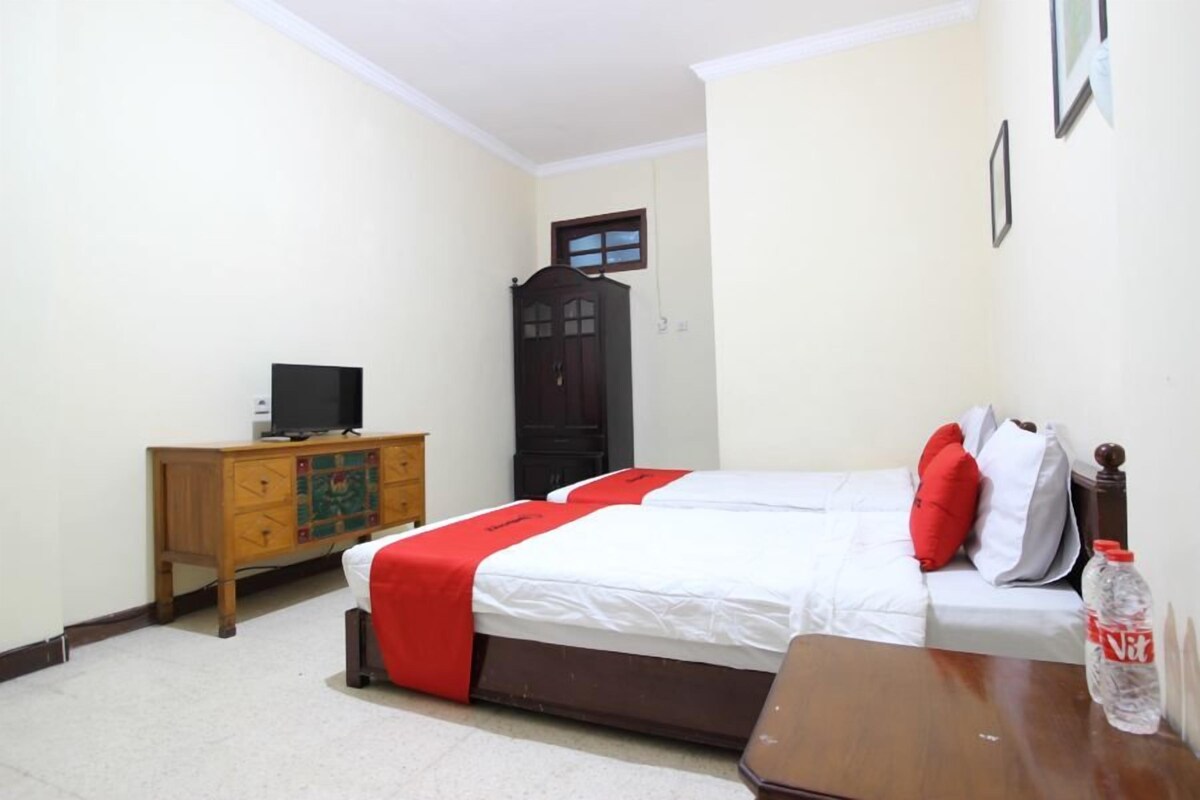 A bedroom with a bed, a wooden dresser, a television, and a door.