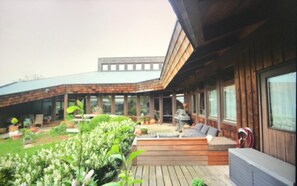 Ein modernes Haus mit überdachter Terrasse, Sitzgelegenheiten im Freien und einem Garten.