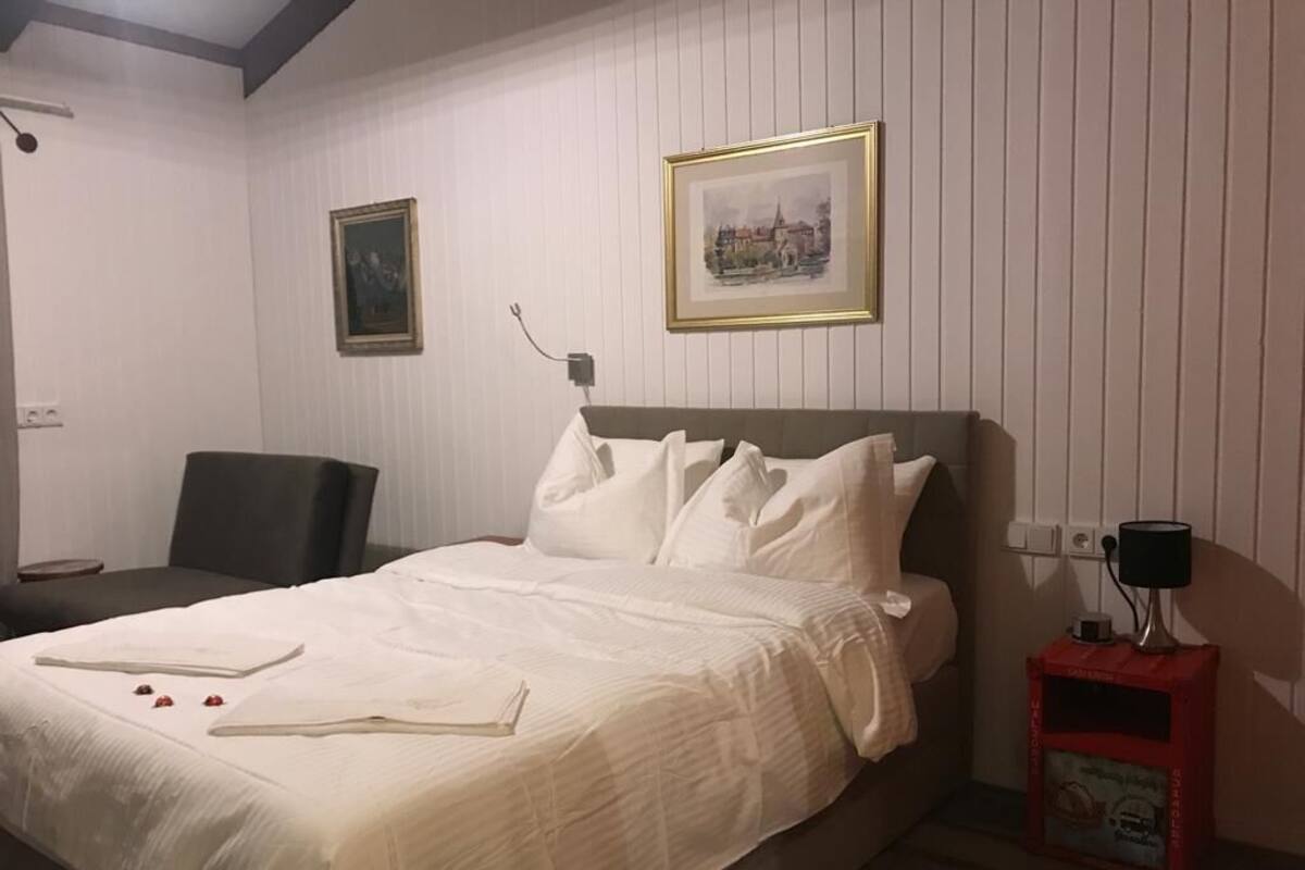 A neatly made bed with white linens, a bedside table with a lamp, and two framed pictures on the wall.