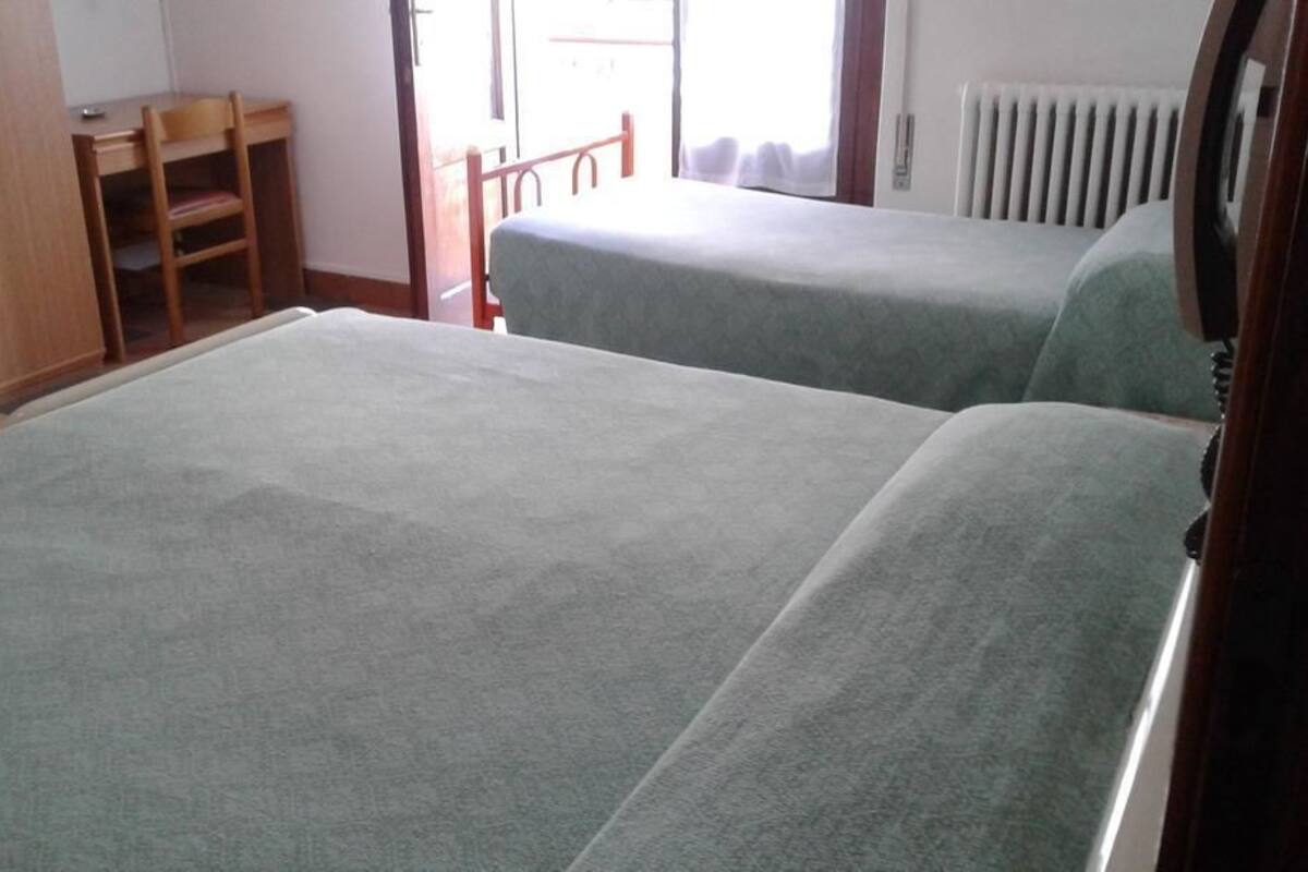A room with two beds, a wooden desk, a chair, and a radiator.