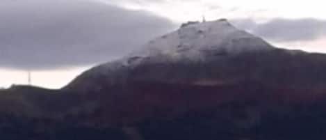 A mountain with a snow-capped peak and a cloudy sky.