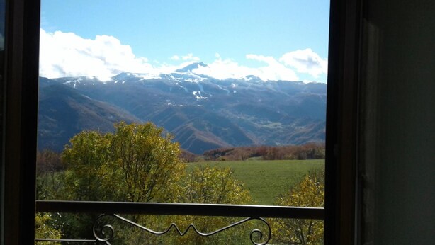 A view from a balcony with a metal railing, overlooking a valley with mountains in the distance and a tree in the foreground. - Hotel Conca D'Oro (Lama Mocogno)