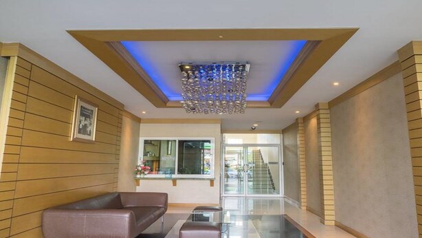 A modern lobby with a brown leather sofa, a small ottoman, and a decorative chandelier. - Sansuk Apartment (Pathum Thani)