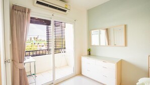 A hotel room with a sliding glass door leading to a balcony, a white dresser, and a mounted mirror. - Sansuk Apartment (Pathum Thani)