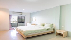 A modern bedroom with a large bed, a bedside table, a window with blinds, and a ceiling fan. - Sansuk Apartment (Pathum Thani)