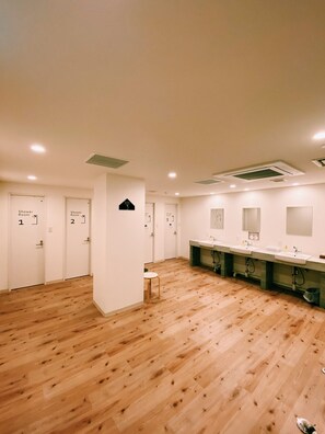 A spacious bathroom with multiple shower rooms, wooden floors, and a row of sinks. - Otaru YaDo - Hostel (Otaru)