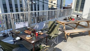 A balcony with a table set for dining, camping chairs, a picnic table, and a suitcase. - Otaru YaDo - Hostel (Otaru)