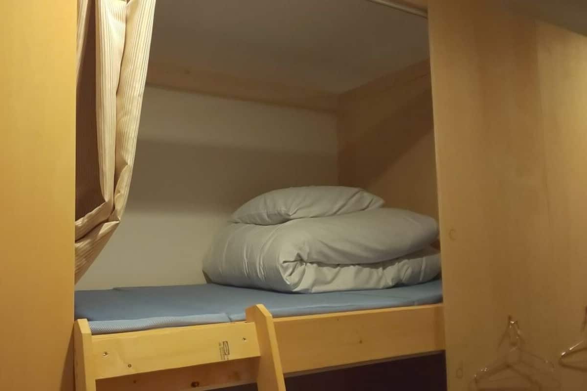 A bunk bed with a mattress and pillows, a wooden ladder, and a small drawer.
