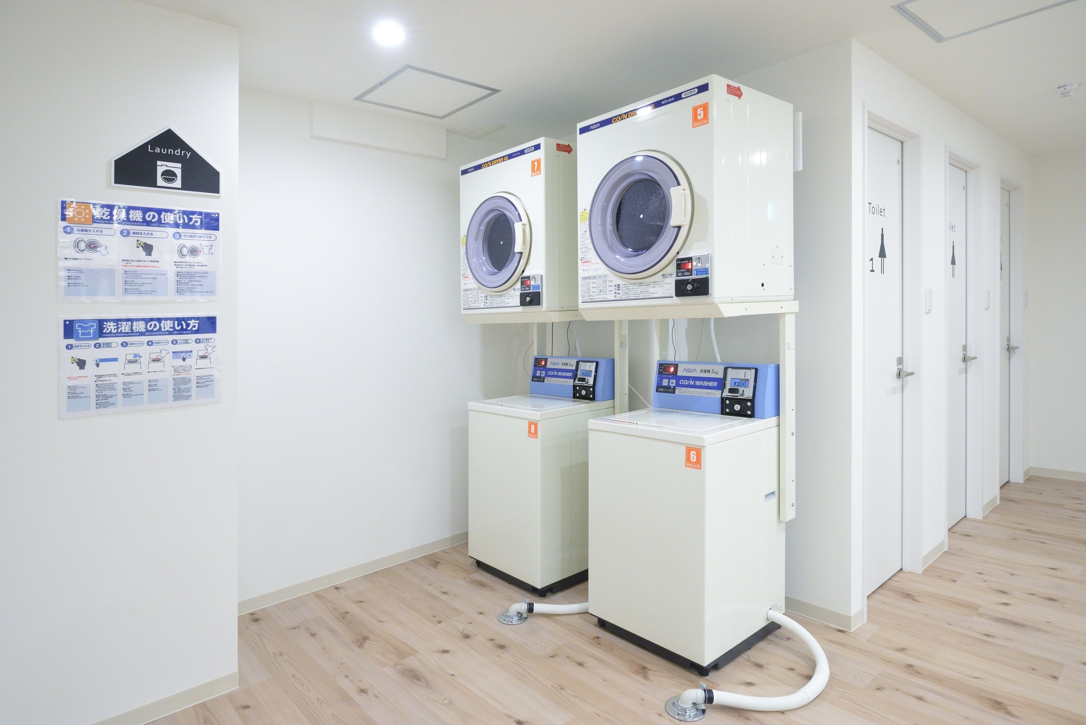 A laundry area with two washing machines and dryers, a sign indicating the location, and a set of instructions on the wall.
