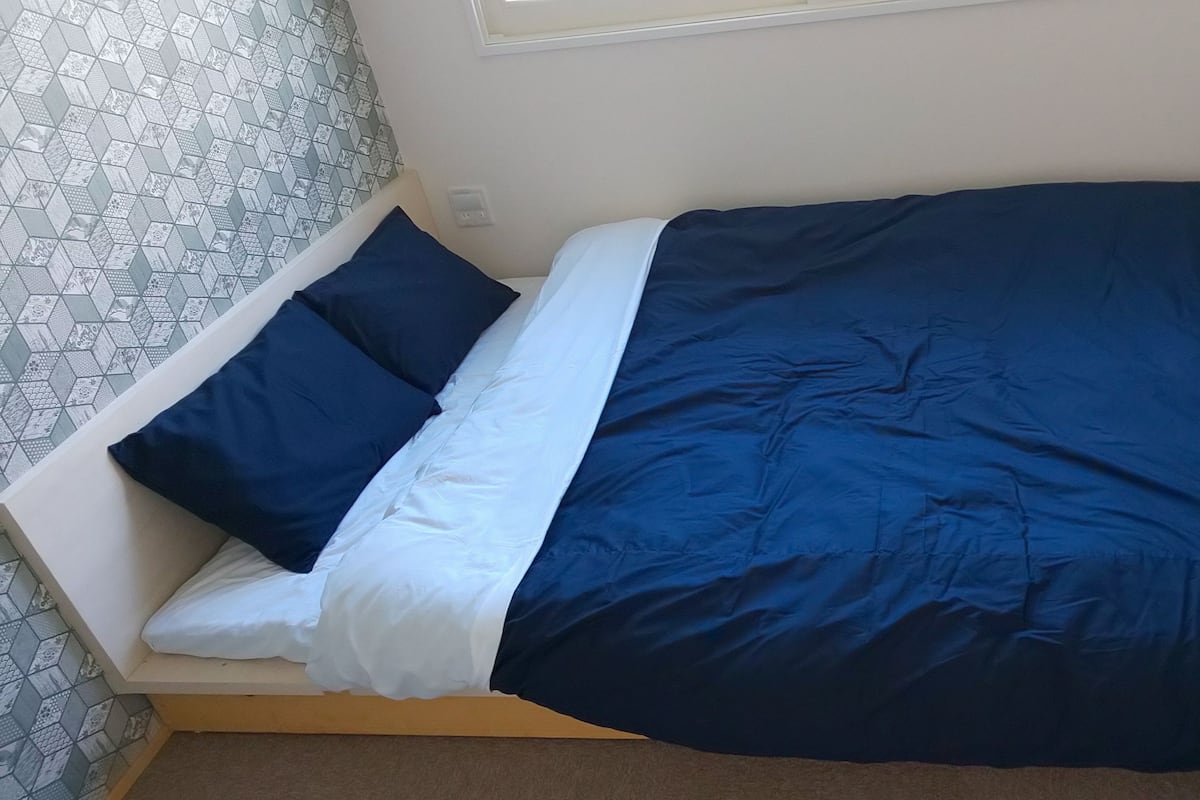A bed with a blue and white bedspread, a dark blue pillow, and a white pillow.