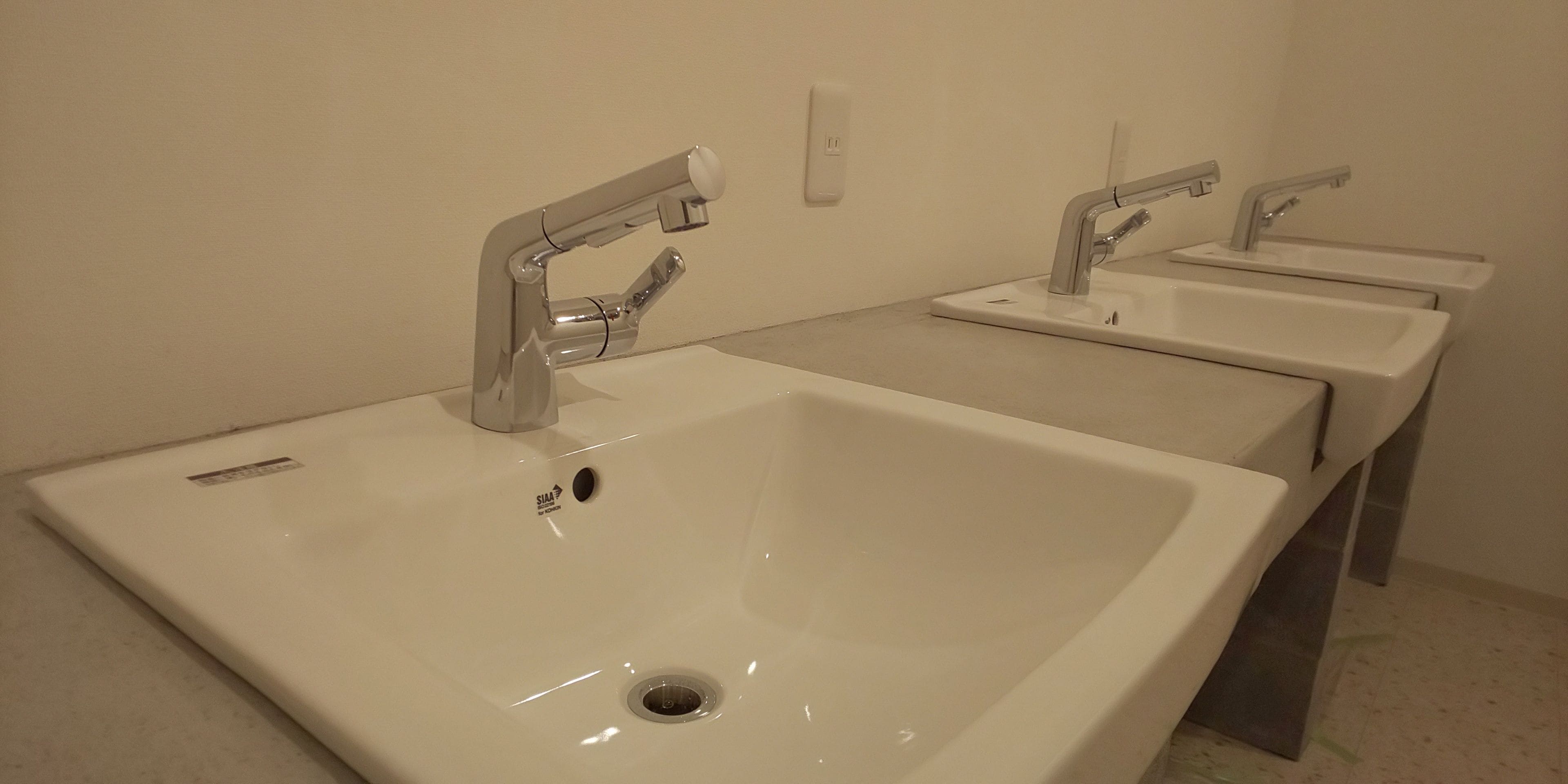 A row of three white sinks with modern faucets in a clean, minimalistic bathroom.