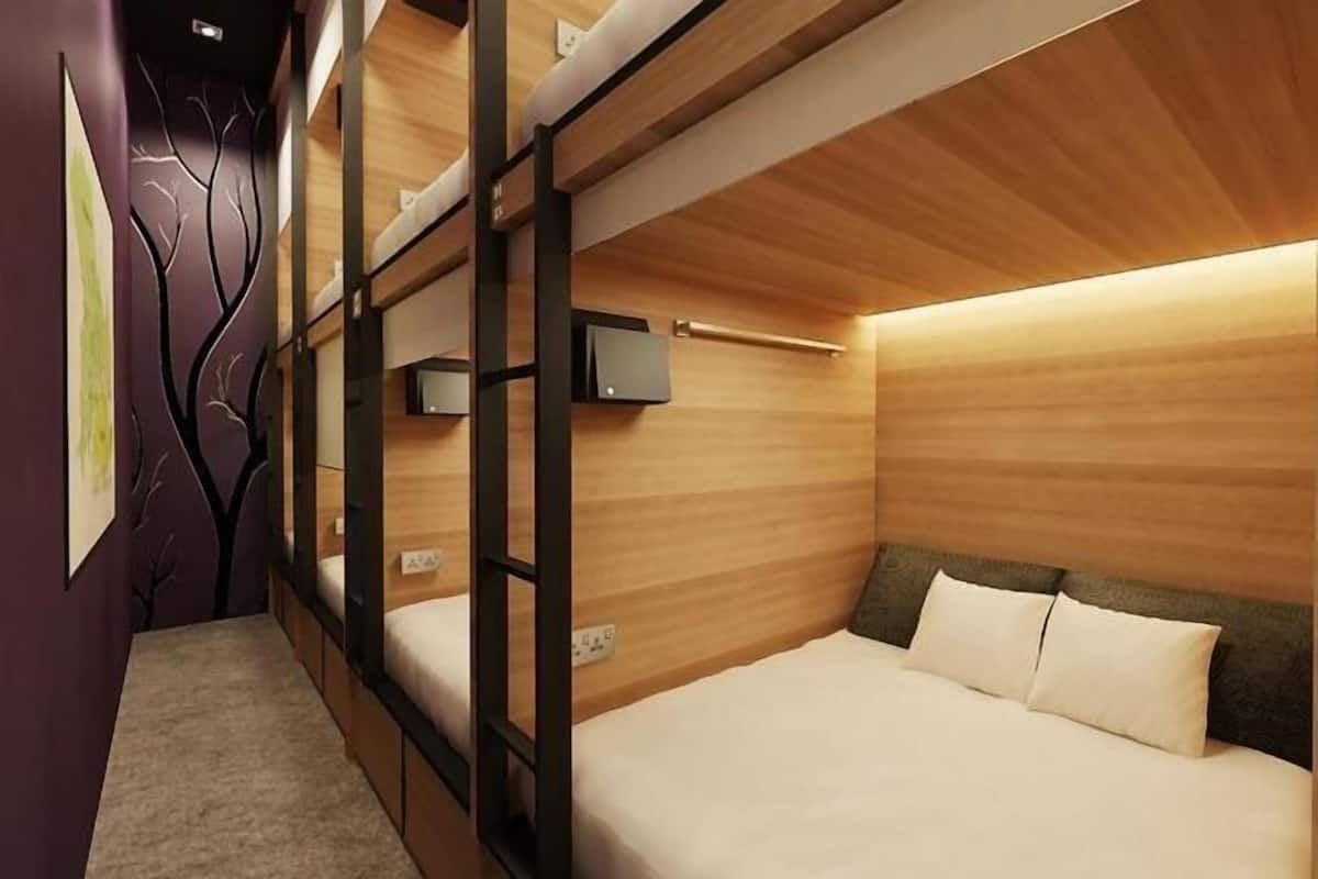 A compact hotel room with bunk beds, a small bedside table, and a wall-mounted TV.